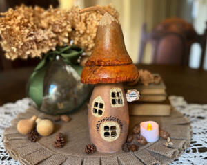 A mushroom fairy house made from dried gourds. It has an orange roof, carved windows, a Rabbit Chateau House sign hangs off the side.